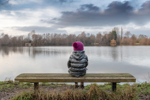 Une petite fille assise sur un banc contemple le lac.