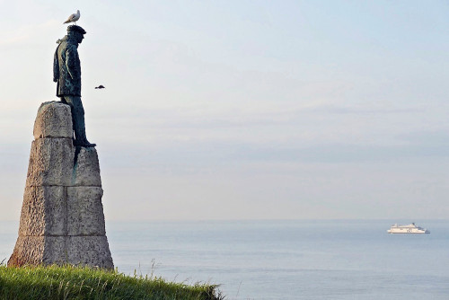 La statue est érigé sur un piédestal et contemple la mer.
